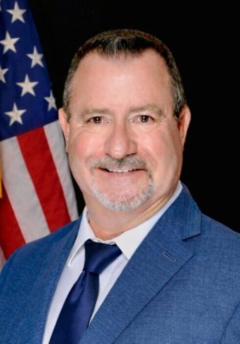Salt-and-pepper goateed man, American flag backdrop